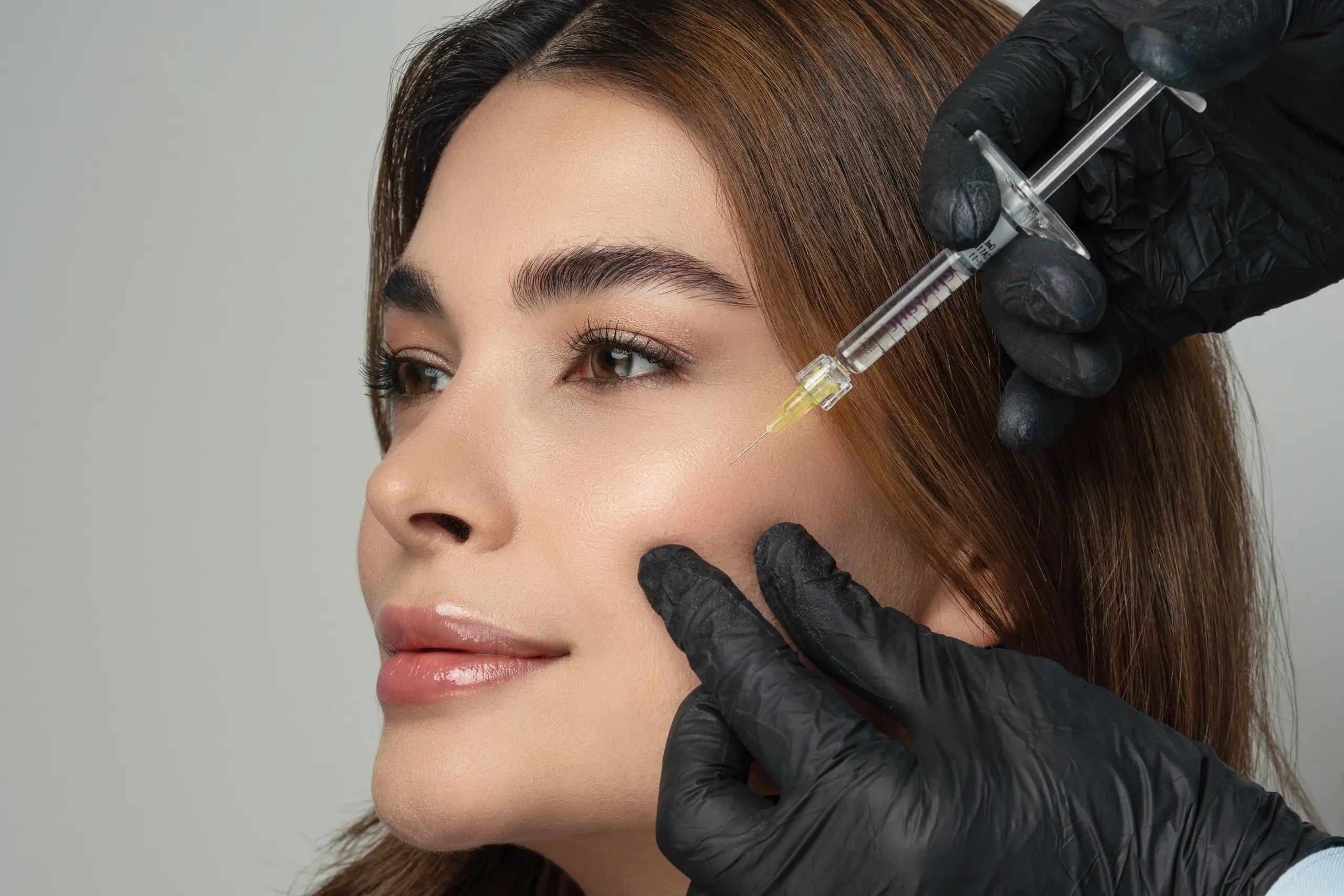 Specialist in black gloves giving an injection in a woman’s cheek area – injectable treatments at Dermique, Sofia